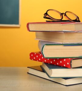 stack-books-with-glasses-wooden-desk-colorful-wall-blackboard-background_392895-523917